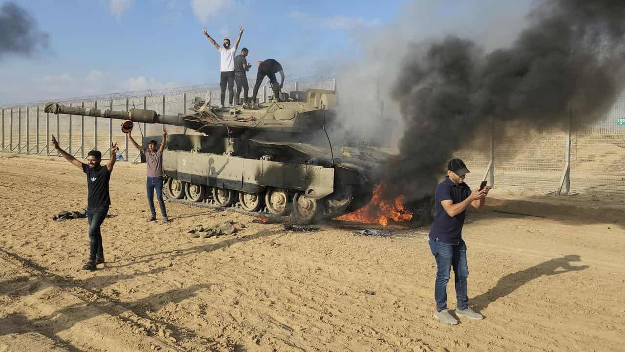 Palestinian fighters on an Israeli tank in flames