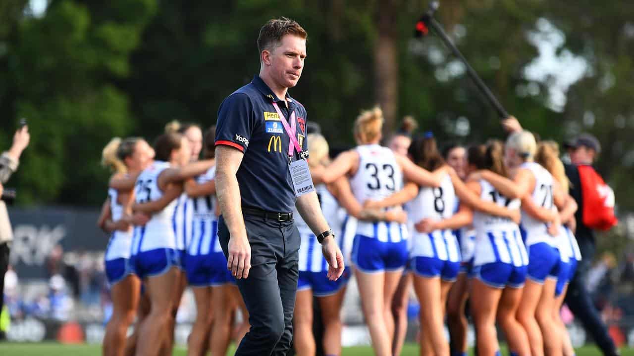 Mick Stinear walks past North Melbourne's celebrating huddle.