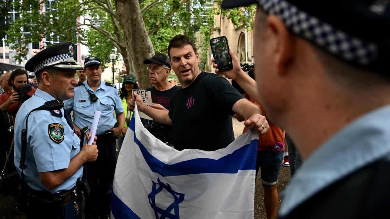 A man with an Israeli flag is spoken to by police.