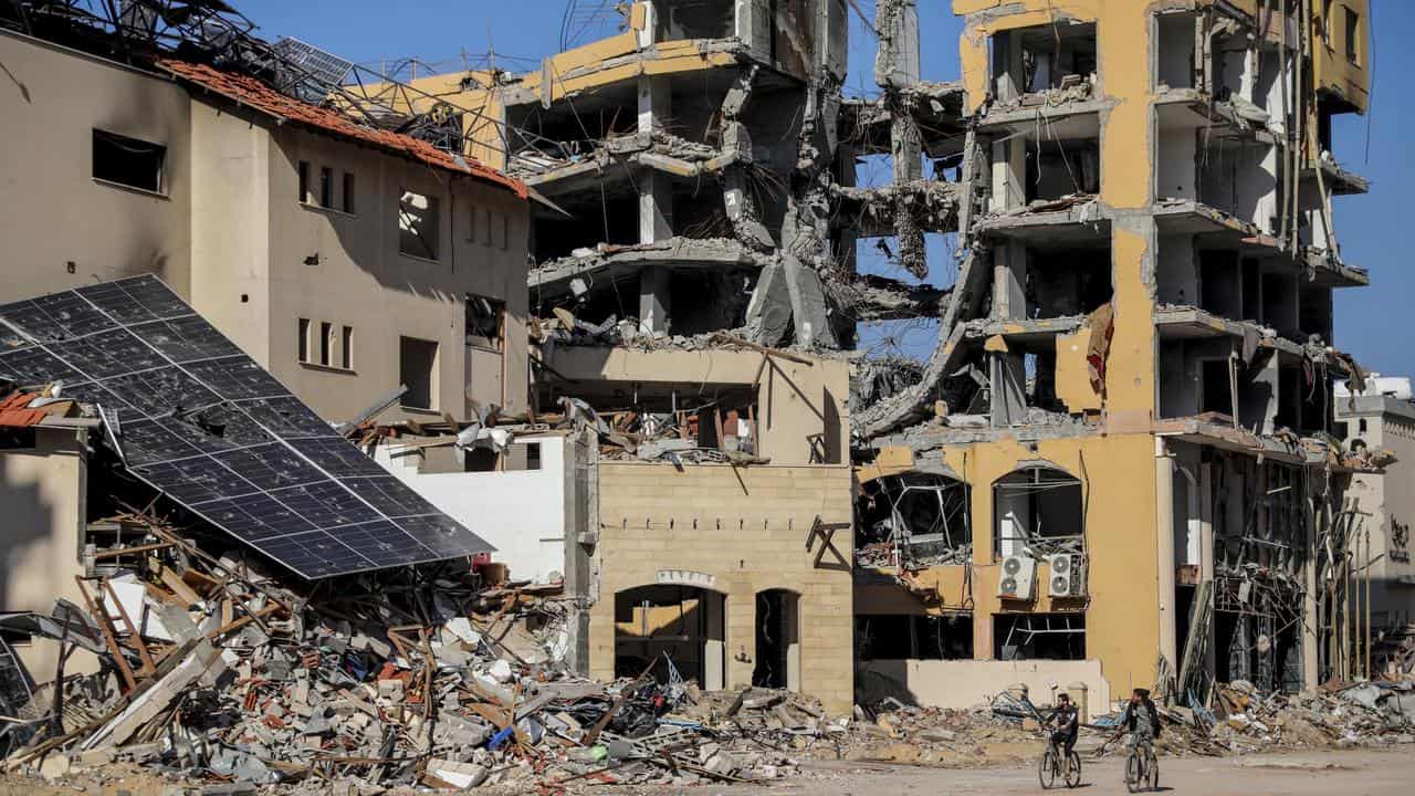 Palestinians ride bicycles by destroyed buildings in Gaza City