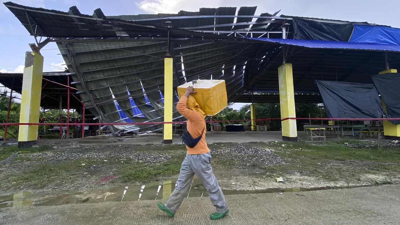 A fish vendor passes by a partially collapsed building