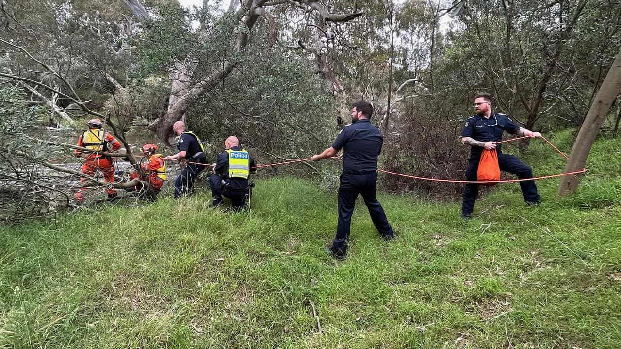 Emergency workers rescuing a woman and her dog from rapid waters