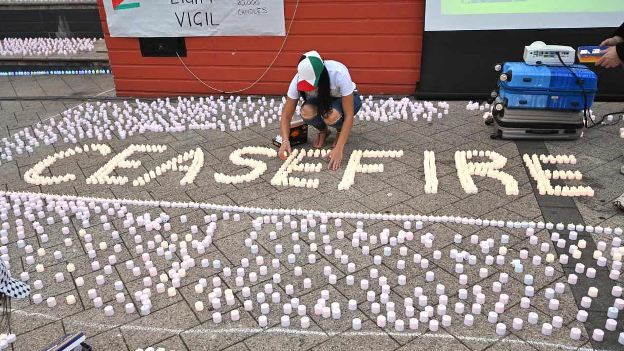 Woman lights candles spelling the word 'ceasefire'.