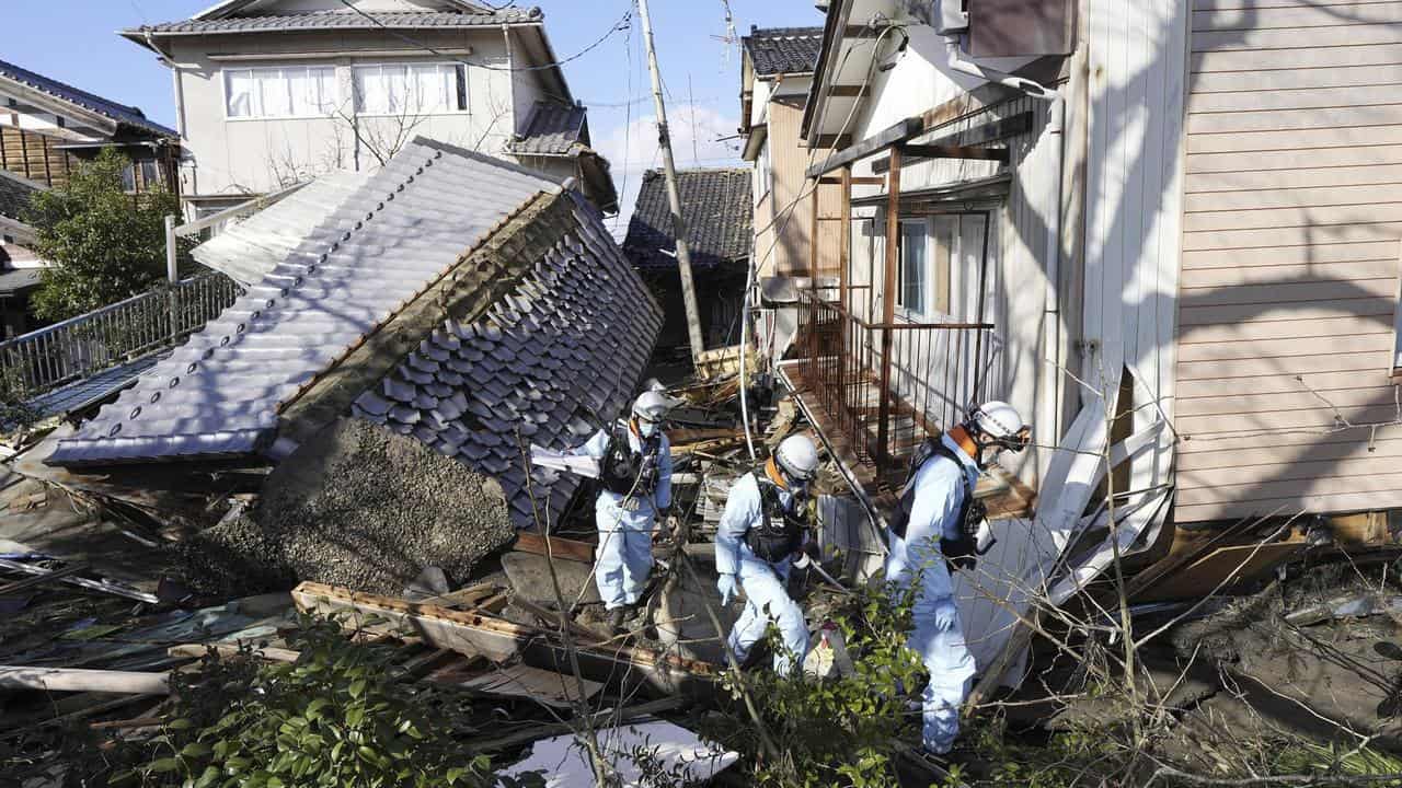 Firefighters walks through fallen houses hit by earthquakes in Japan