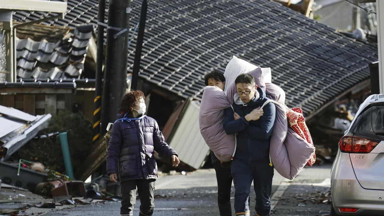 People carry bedclothes through fallen houses hit by earthquakes