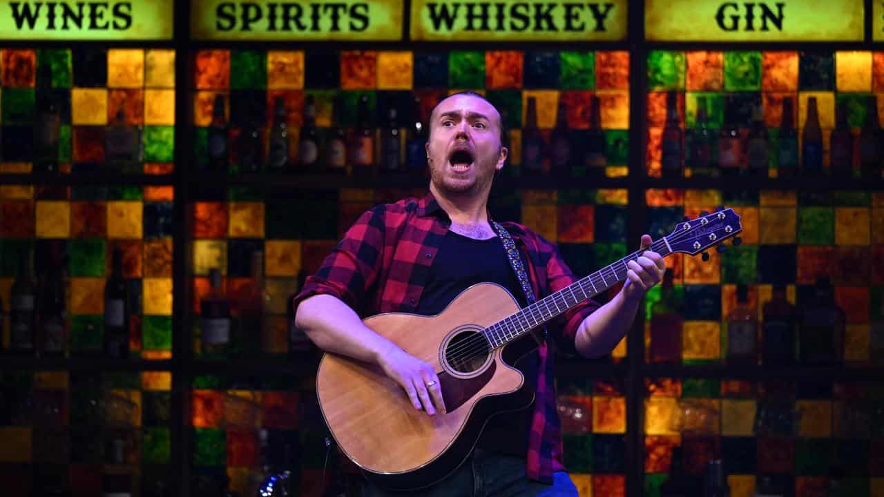 A cast member performs with a guitar.