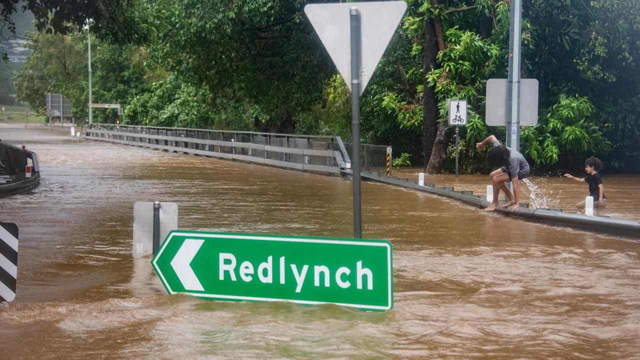 Children walk through floodwaters near Redlynch in Cairns.