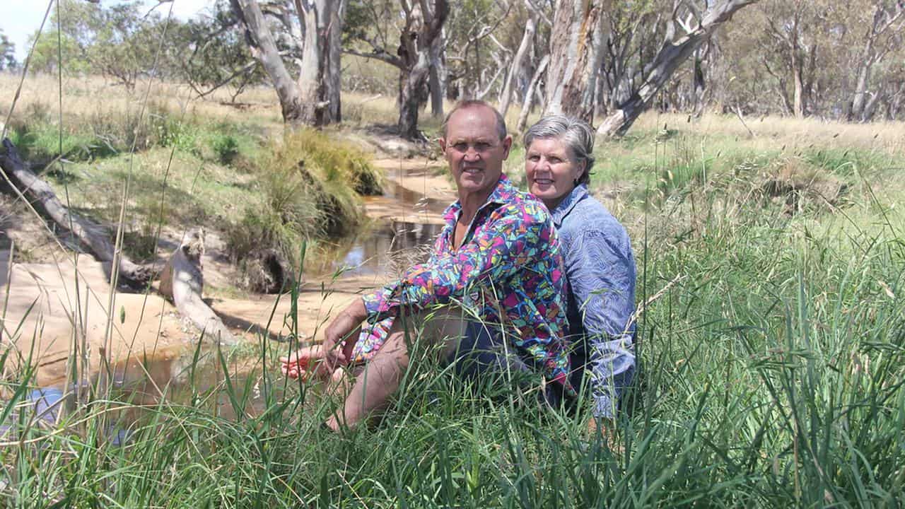 James and Donna Winter-Irving sit in grass near creek