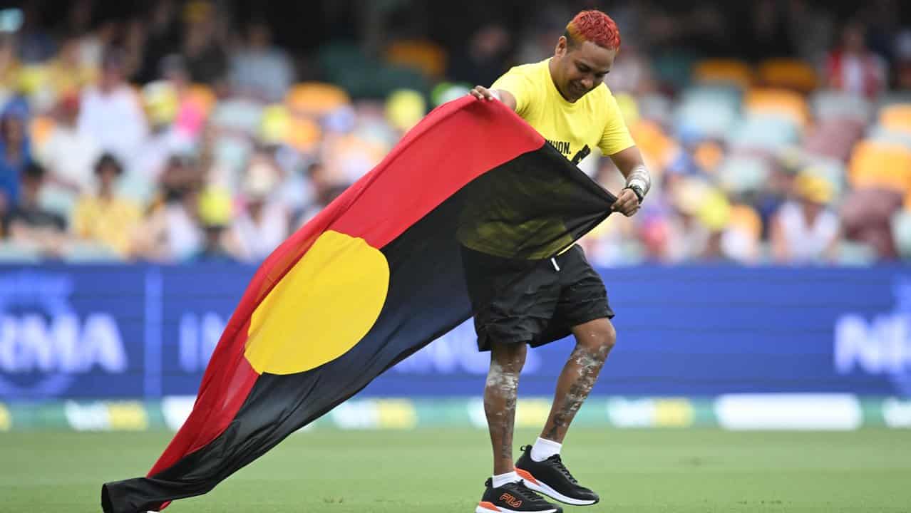 A man carries an Aboriginal flag onto the playing surface at the Gabba