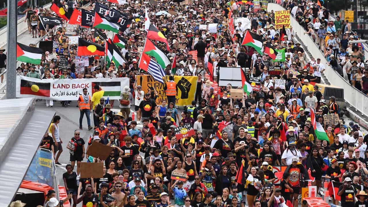 A crowd of people march down the street, holding flags and signs 