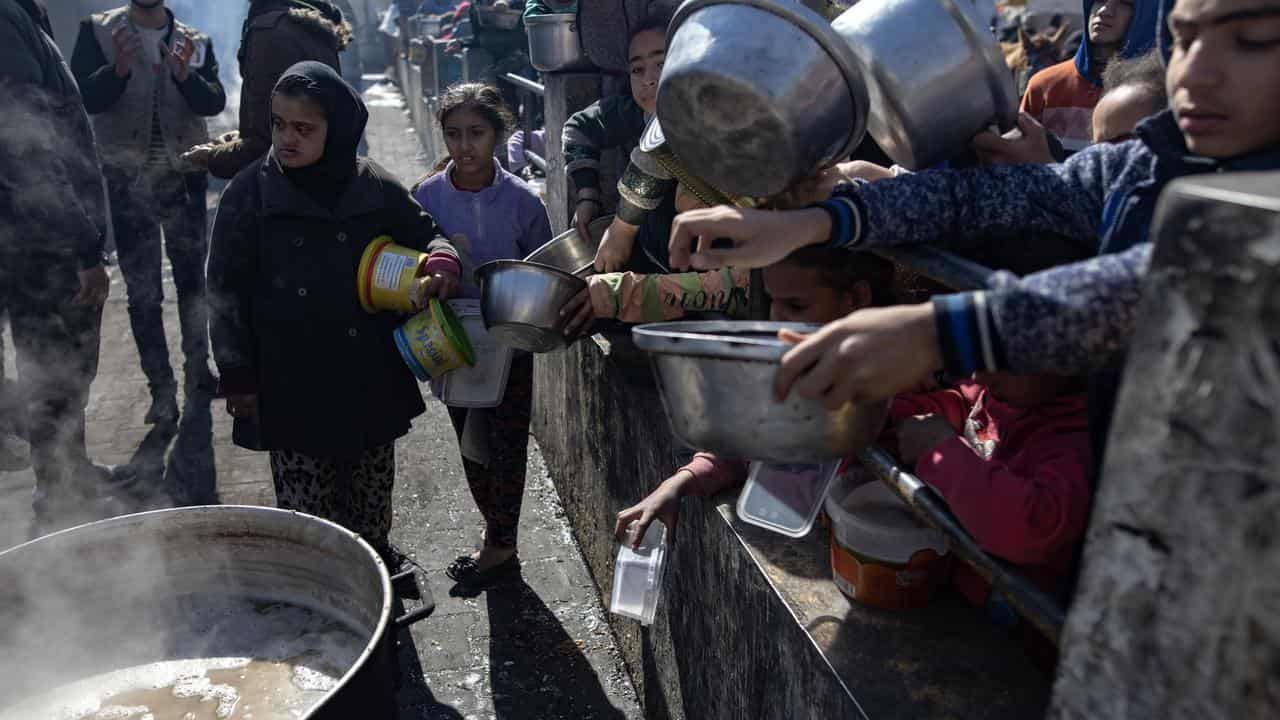 Displaced Palestinians line up to receive food aid in Rafah