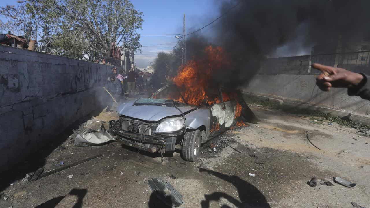 Palestinians watch a car burn after it was hit by an Israeli strike