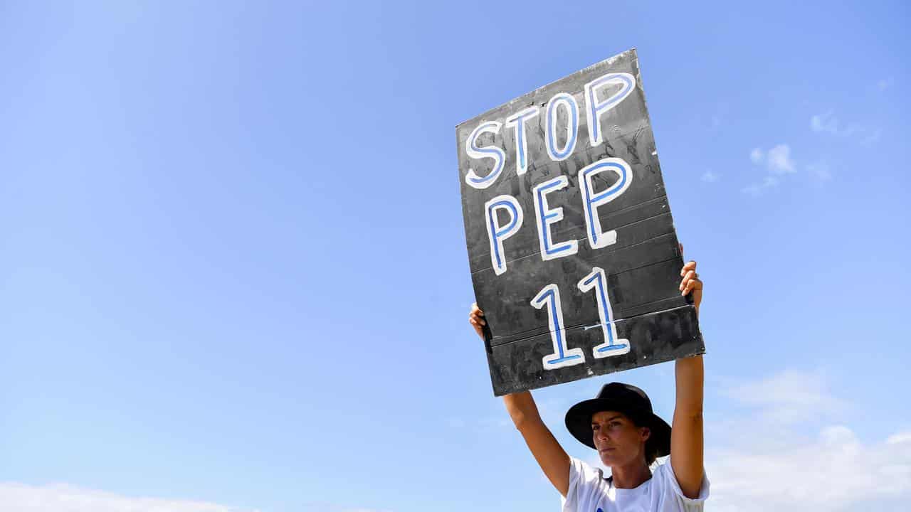 Woman holds placard aloft saying STOP PEP 11