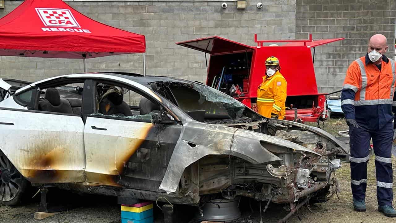 Responders examine the burnt-out wreck of a Tesla Model 3