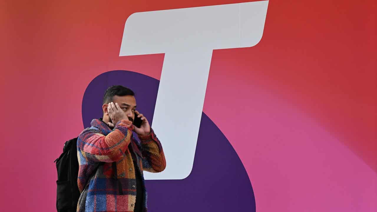 A man is seen using his mobile phone as he walks past Telstra signage