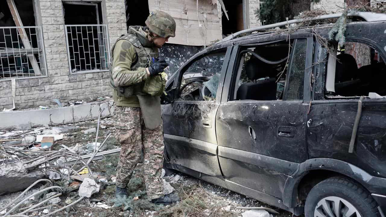 A Ukraine soldier looking at a car damaged by a rocket attack