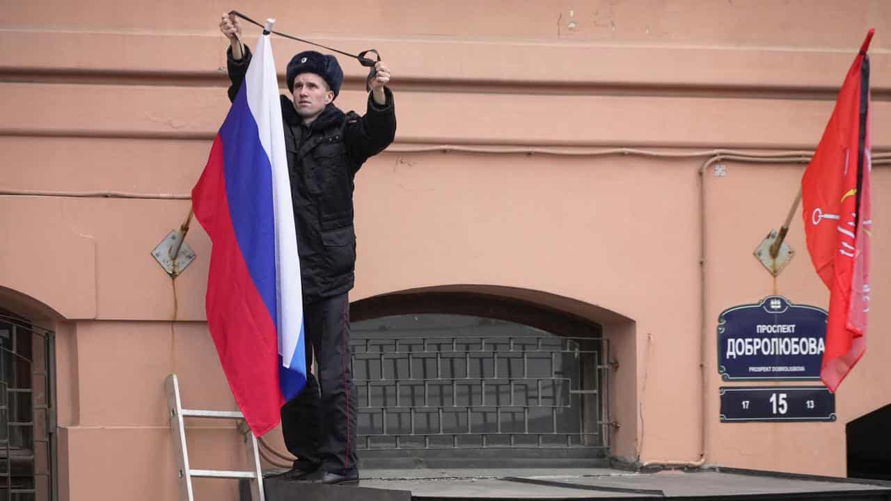 A police officer ties a mourning ribbon to a Russian flag i