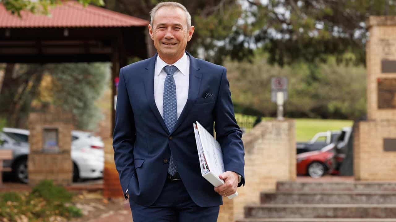 Premier Roger Cook walking while carrying a folder.