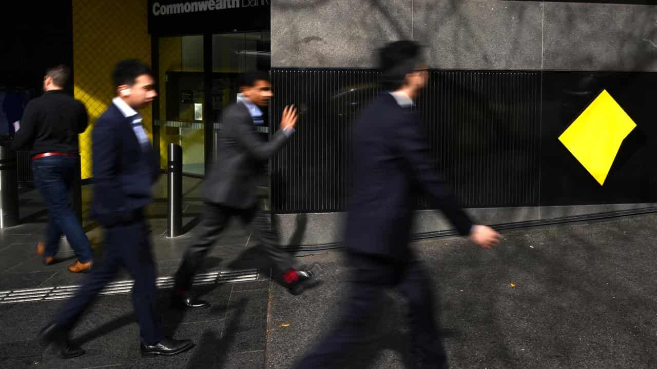 Men in suits walking past a Commonwelth Bank branch.