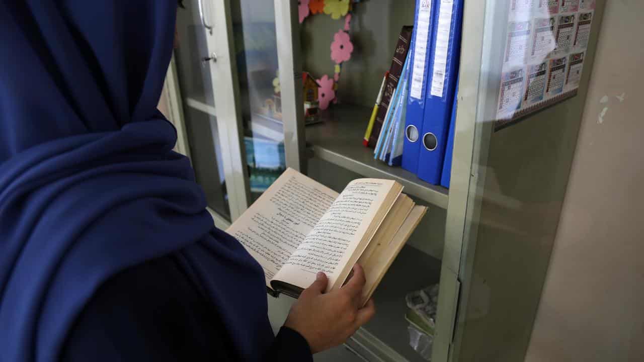 An Afghan girl reads a book in her home.