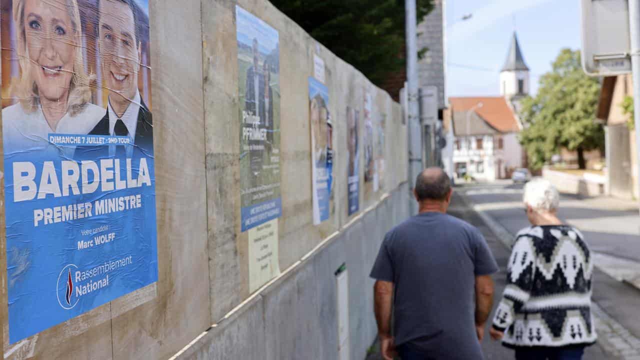 People walk past election posters in France