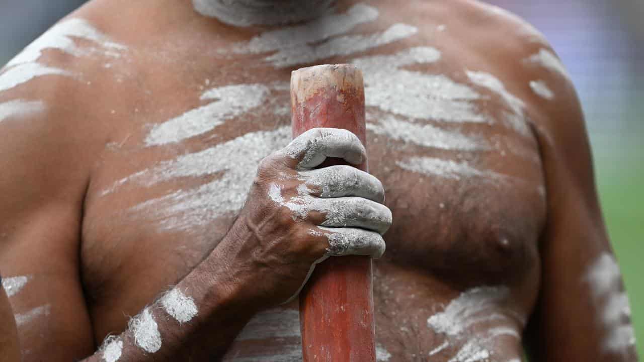 An Indigenous Australian man holding a Didgeridoo