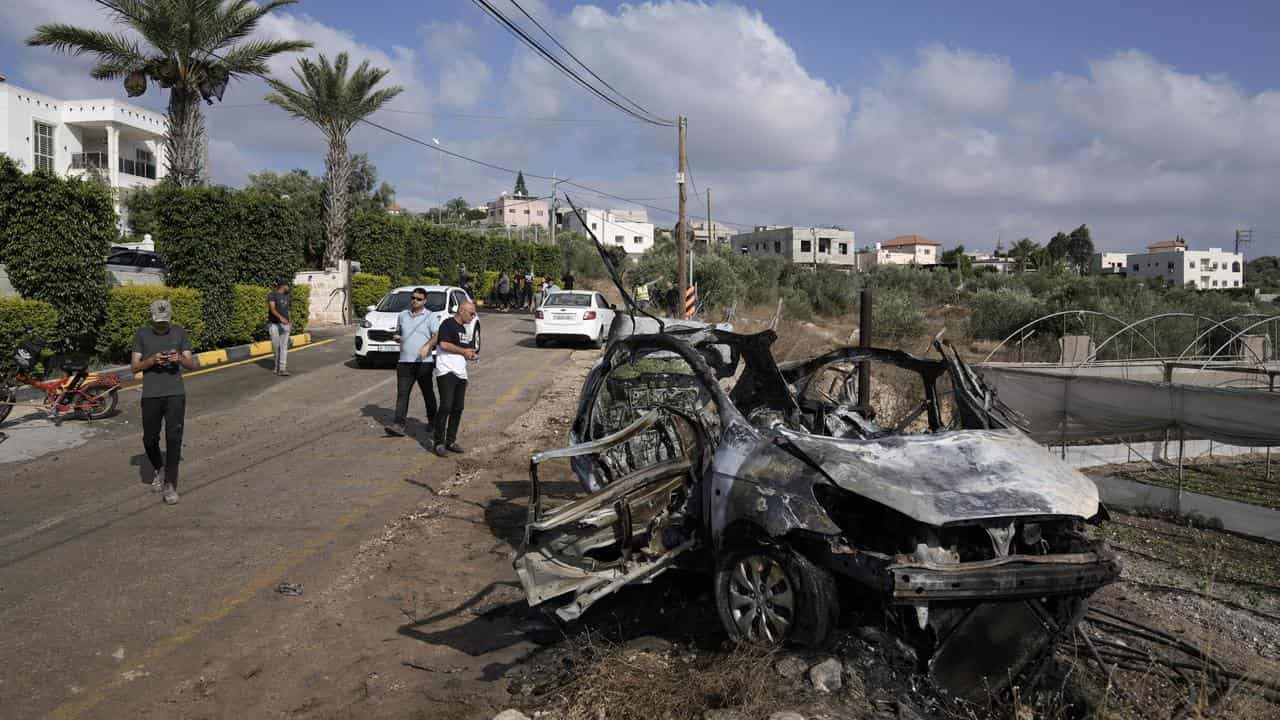 Palestinians gather around a car destroyed in a drone strike