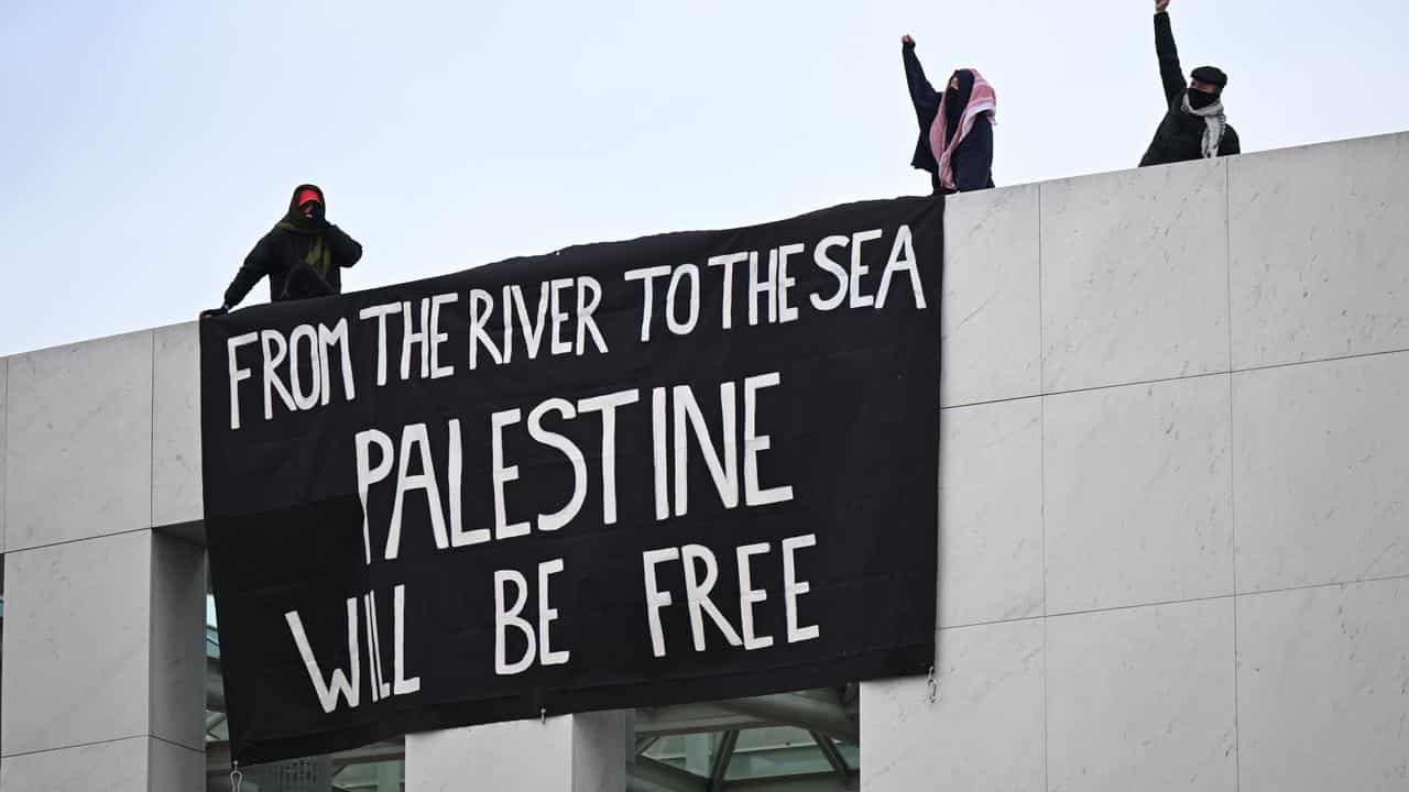 Pro-Palestine protesters hang banners from the top of Parliament House