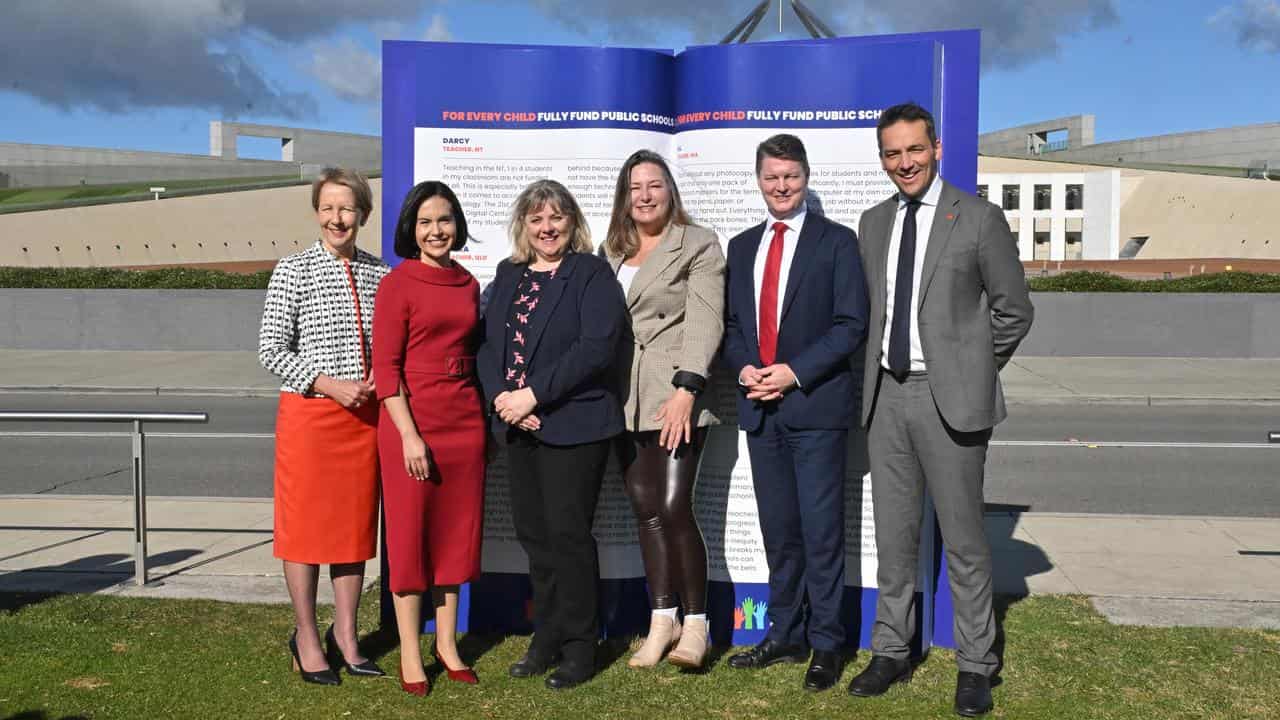 Education ministers and officials stand in front of parliament house.