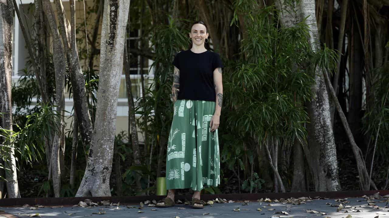 A woman stands in front of some trees.