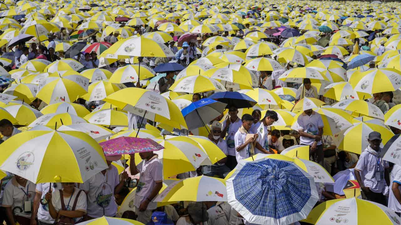 The faithful shield themselves from the sun waiting for the Pope