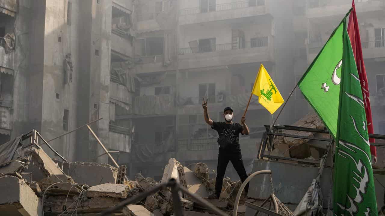 A man holding up a Hezbollah flag amid ruins in Lebanon.