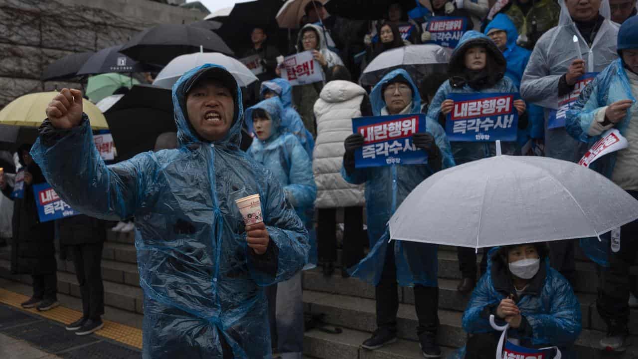 Protesters wait in the rain for a candlelight vigil in Seoul