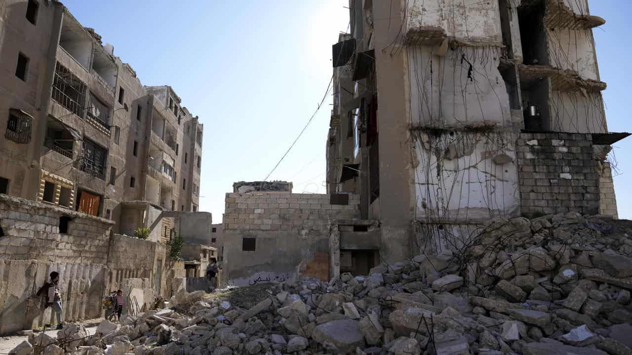 Syrian children play next to a destroyed residential building