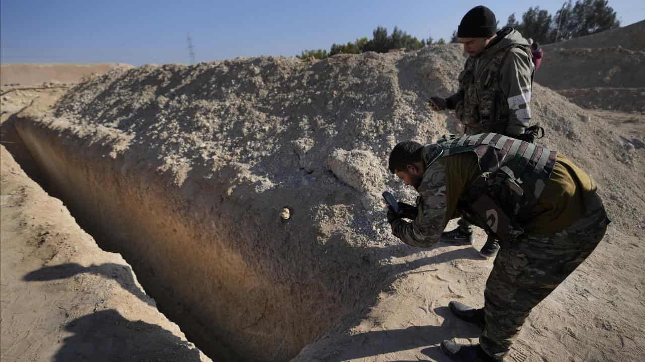 Syrian fighters observe a location identified as a mass grave