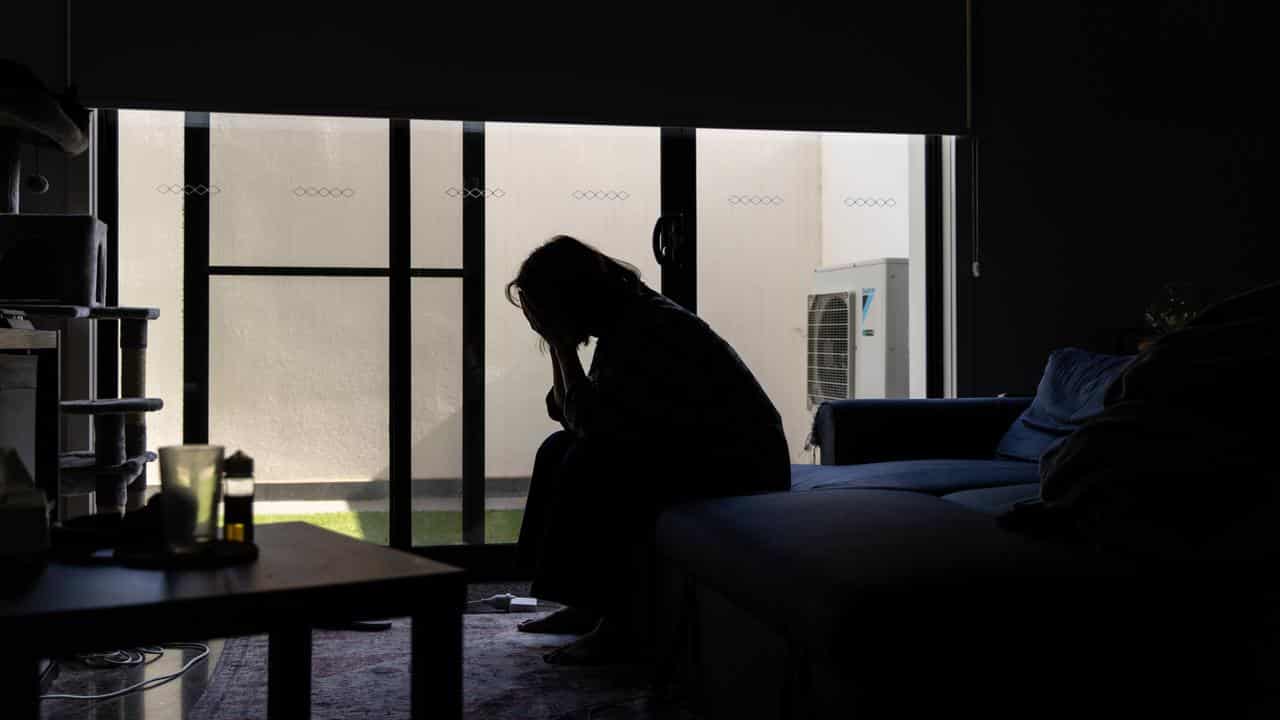 Woman holds head in hands in darkened room