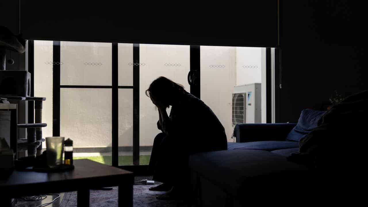 Woman holds head in hands in darkened room