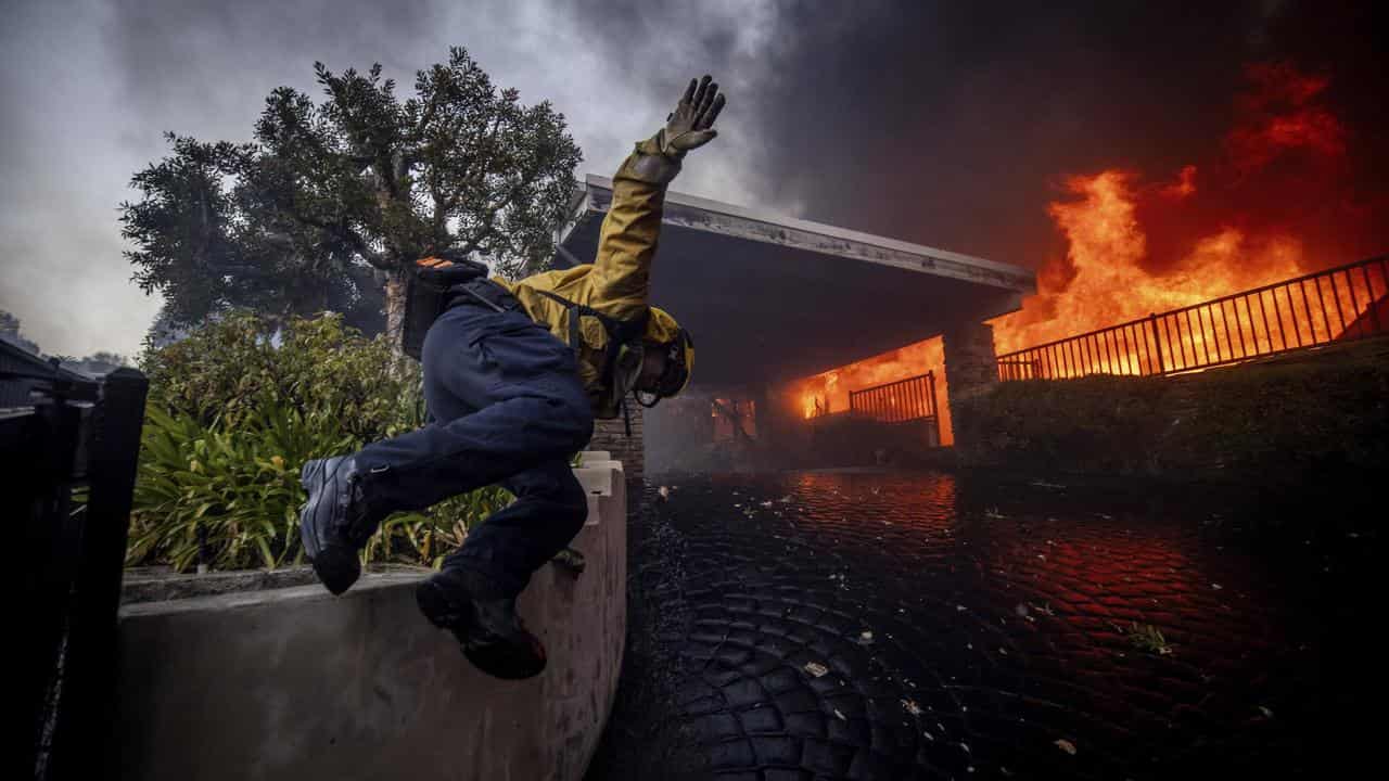 A firefighter jumping over a fence while fighting the Palisades fire