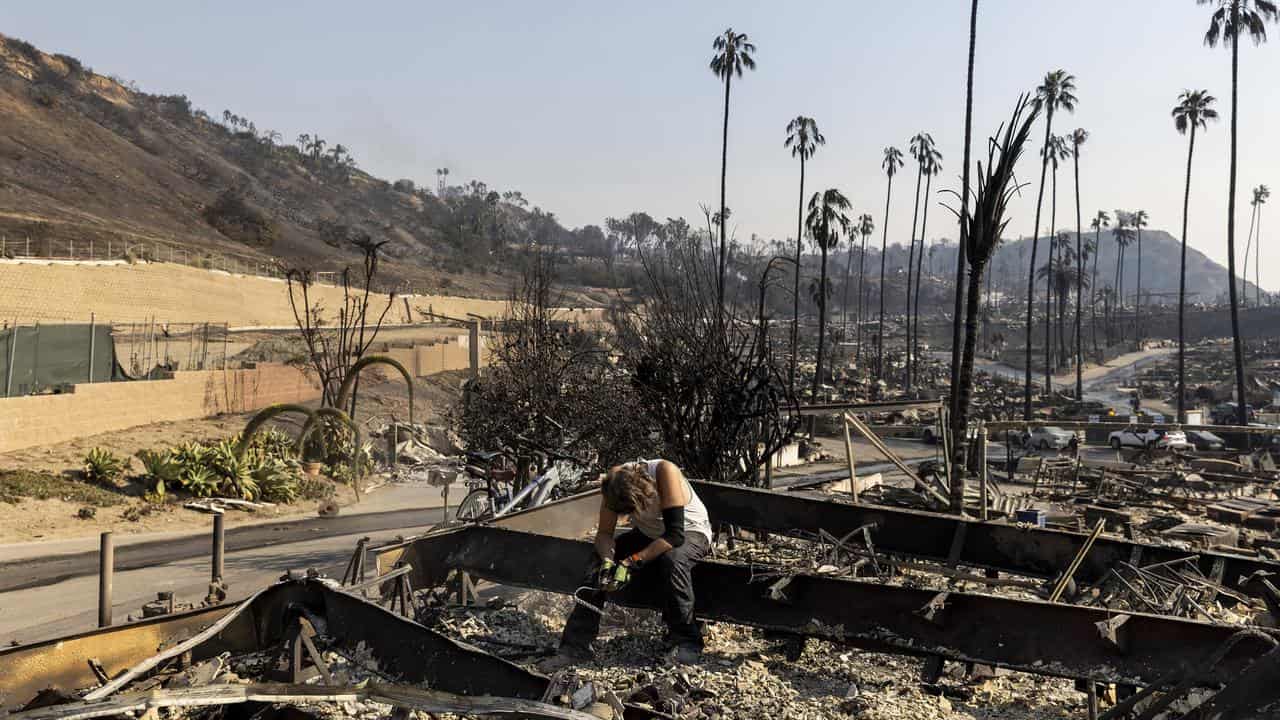 A man pauses as he searches in a burned house in Pacific Palisades