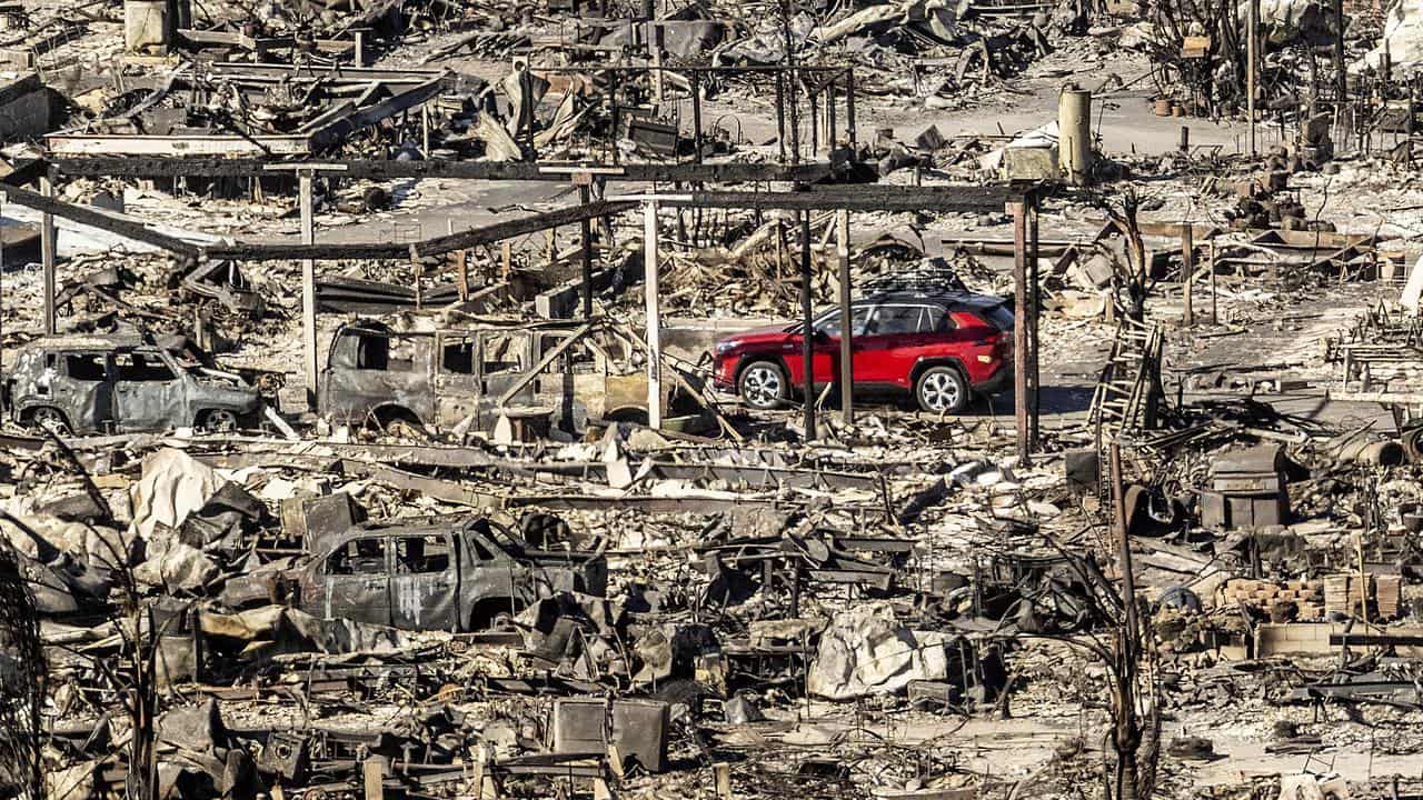 A car drives past homes and vehicles destroyed by the Palisades Fire