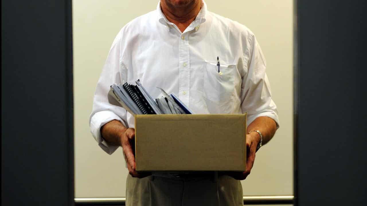 Office worker stands in a lift holding a box of office supplies.