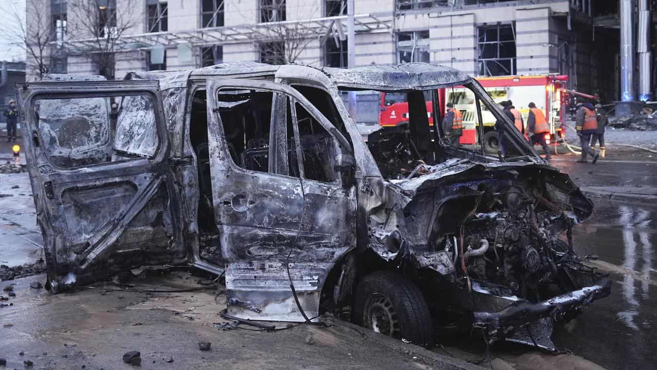 Destroyed car and firefighters working on a damaged building