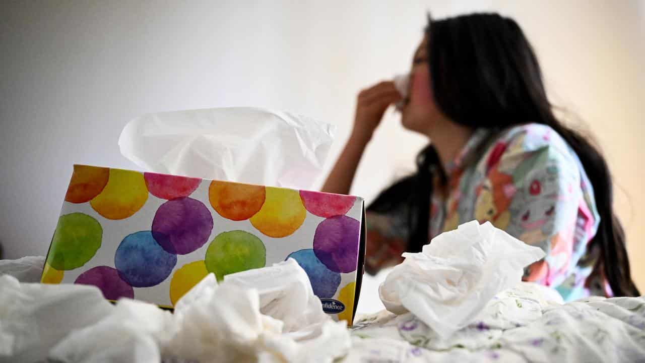 A young woman uses tissues as she recovers from the flu 