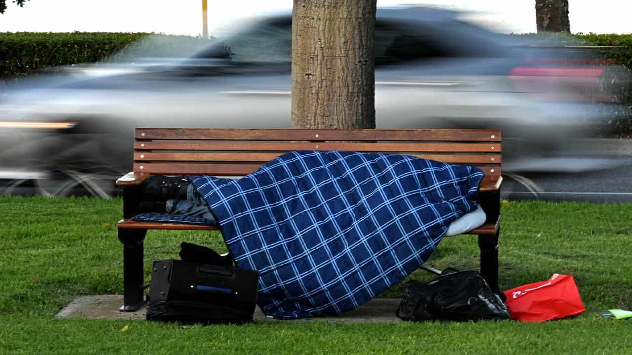 A homeless person is seen sleeping on a park bench