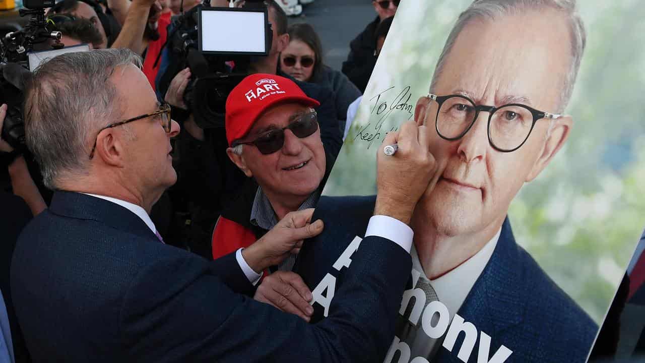 Anthony Albanese signs an election campaign poster in 2022