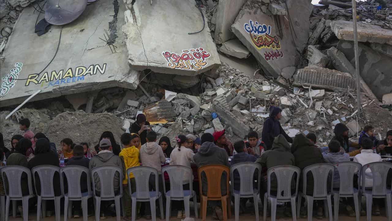 Palestinians at a table surrounded by the rubble of destroyed homes