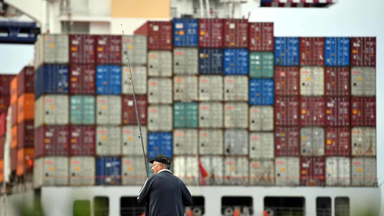 A fisherman is seen in front of a container ship