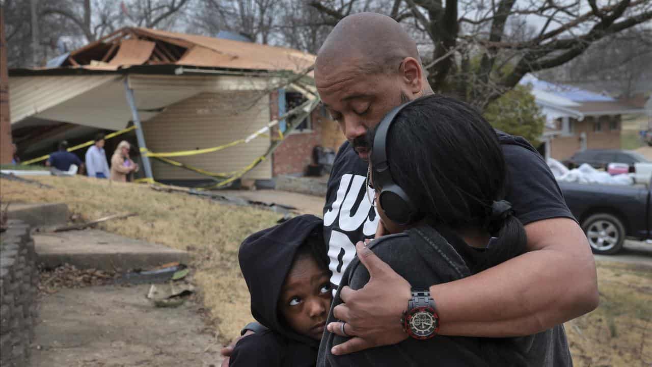 A man embraces his daughters in front of his destroyed home