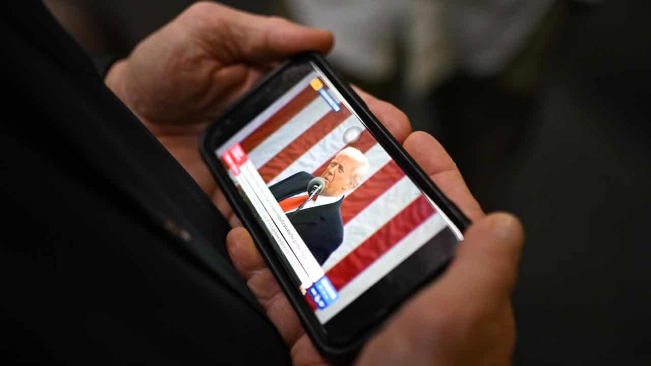 A journalist watches an announcement on tariffs on a mobile phone.
