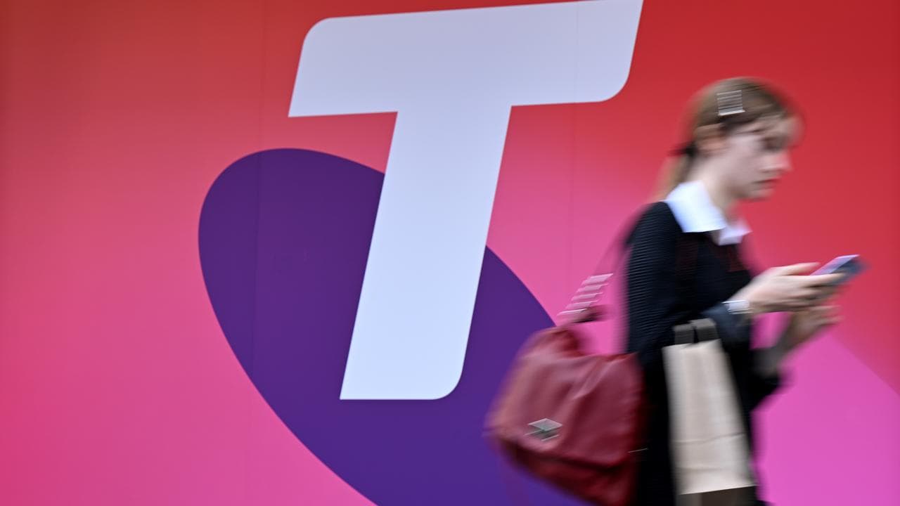 A person uses their mobile phones as they walk past Telstra signage